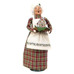 Grandmother with white cap and apron holding gingerbread house on platter